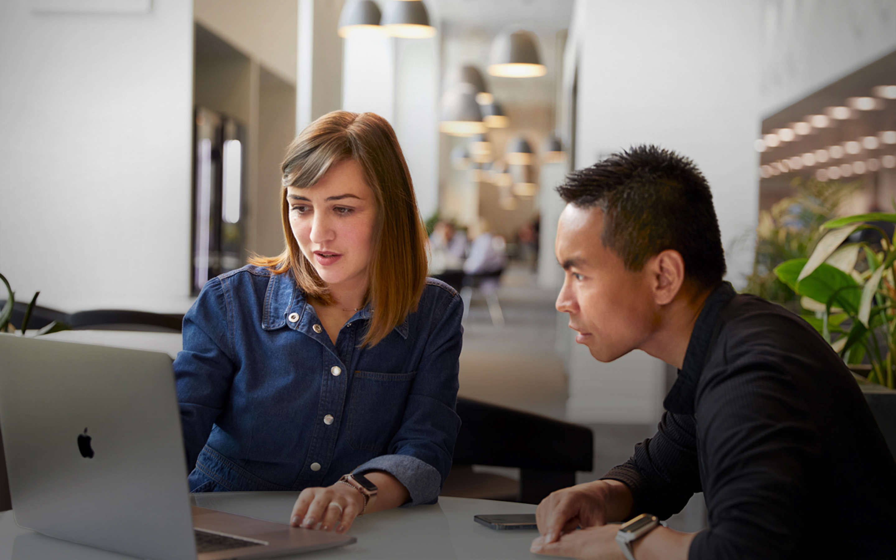Two Apple Support and Service team members looking at a MacBook in a common area.