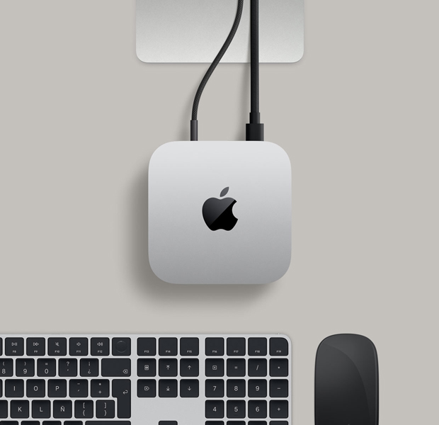 Vista desde arriba de un Mac mini color plata en un escritorio con un disco externo conectado, junto a un Magic Keyboard color plata y blanco, un Magic Mouse blanco y una cámara