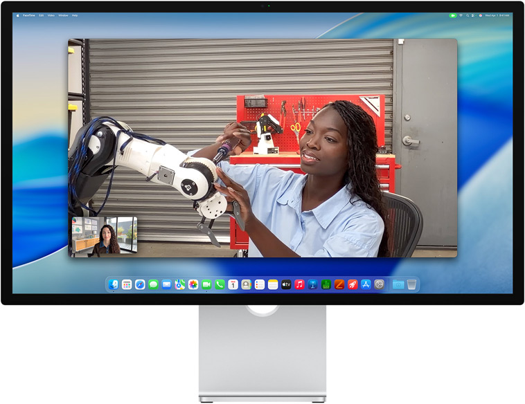 Zwei Personen bei einem Videoanruf auf dem Studio Display, die Automatische Ausrichtung hält sie in der Bildmitte, auch wenn sich eine Person bewegt, um einen Teil des Equipments zu reparieren