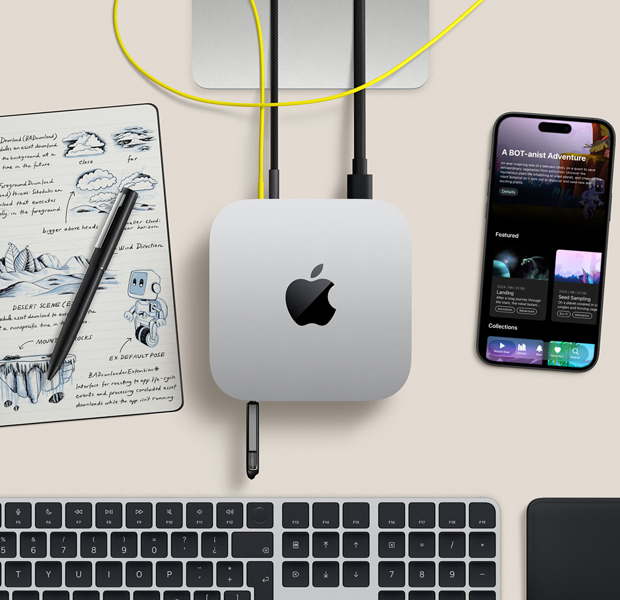 Vista desde arriba de una Mac mini sobre un escritorio con cables y un flash drive conectados en los puertos. Junto a la Mac mini hay un teclado inalámbrico, un trackpad, un iPhone y un bloc de notas.