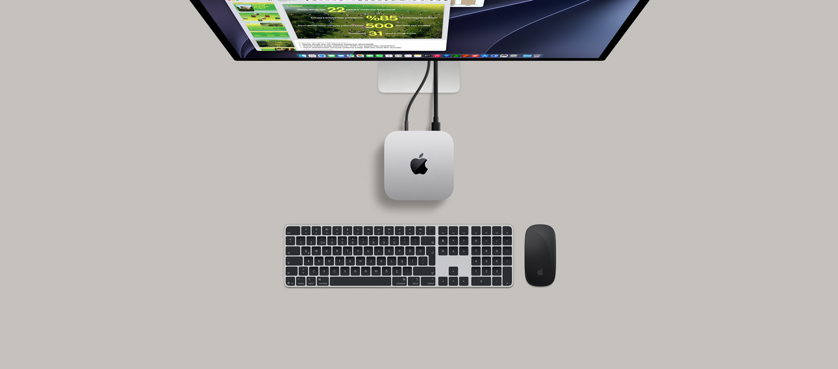Bir ekrana bağlı gümüş rengi Mac mini’nin üstten görünümü, ekranda oyun oynandığı görülüyor ve yanında bir kablosuz klavye, bir oyun kumandası ve mavi bir AirPods Max bulunuyor