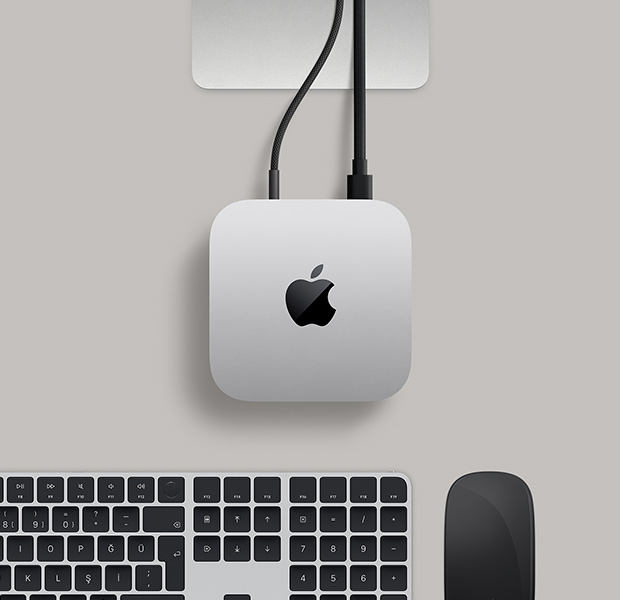 Siyah bir Magic Mouse ve siyah bir Magic Keyboard’un yanında yer alan ve arka bağlantı noktalarına bağlı iki adet kablo ile bir ekrana bağlı olan gümüş rengi Mac mini’nin üstten görünümü
