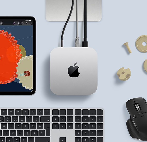 Gümüş rengi Mac mini, siyah ve gümüş rengi kablosuz klavye, siyah bir mouse ve bir iPad’in bulunduğu masa düzeninin üstten görünümü