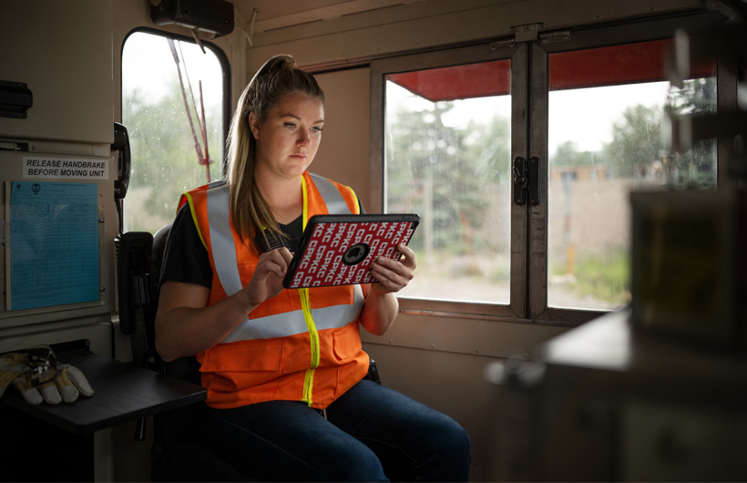 Een spoorwegmedewerkster zit in een stilstaande treinwagon en bekijkt gegevens op een iPad