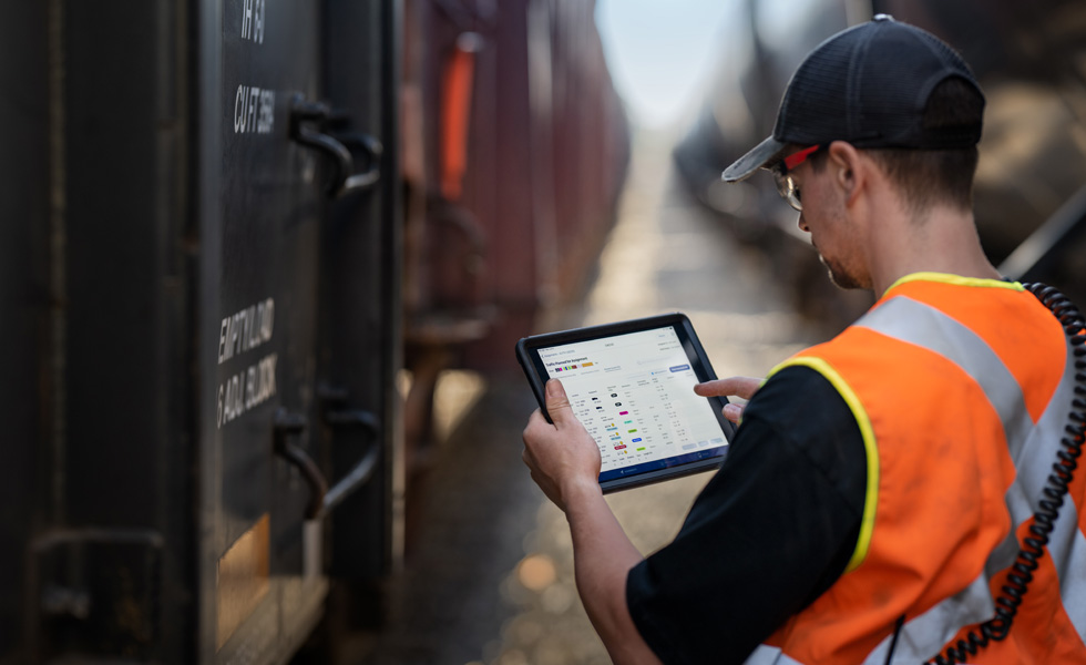Een spoorwegmedewerker staat naast een trein en bekijkt planningsgegevens op een iPad