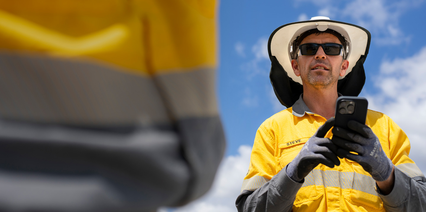 Trabalhador de construção vestido com equipamento de segurança a segurar um iPhone enquanto fala com um membro da equipa