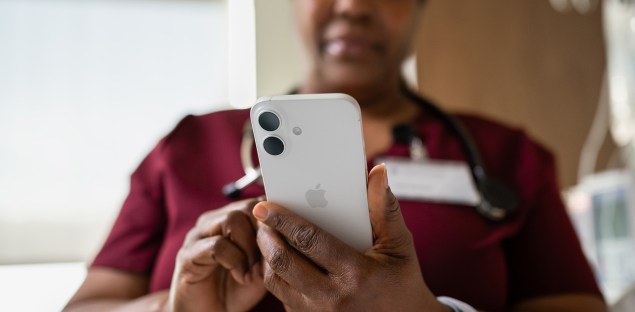 En kvinnlig sköterska i röda sjukhuskläder som tittar på sin iPhone.