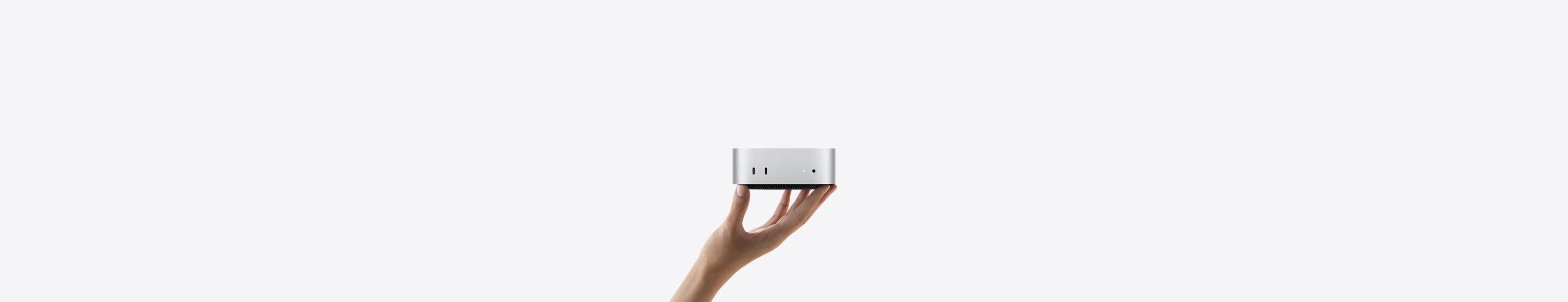 Front view of Mac mini balanced on the fingertips of an up-stretched hand, front shows two Thunderbolt ports, status indicator light and headphone jack, tapered black base at bottom, flat top, rounded sides, straight edges, silver color