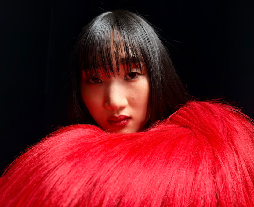 Tampilan close-up seorang perempuan yang memakai atasan bulu merah terang menunjukkan kemampuan fotografi resolusi super tinggi pada iPhone 17 Pro