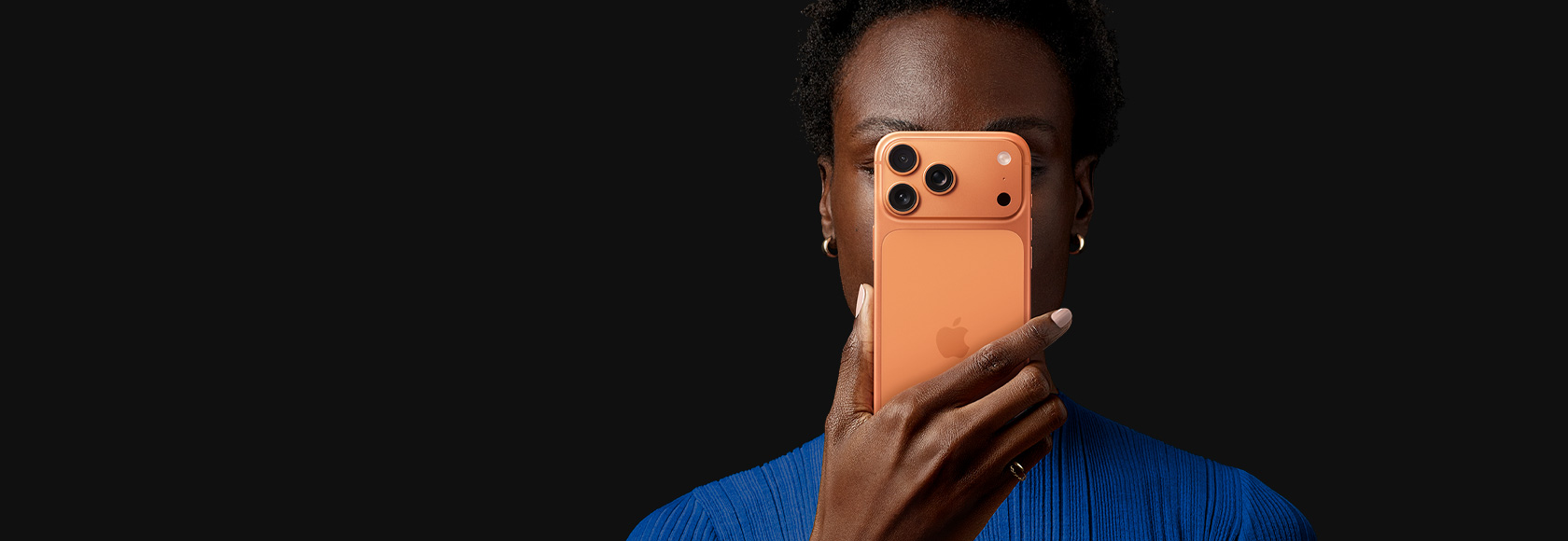 コズミックオレンジのiPhone 17 Proを顔の前で持っている人物。背面を外側に向けている